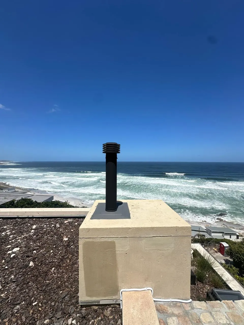 Black cowl on a plastered chimney stack facing the sea