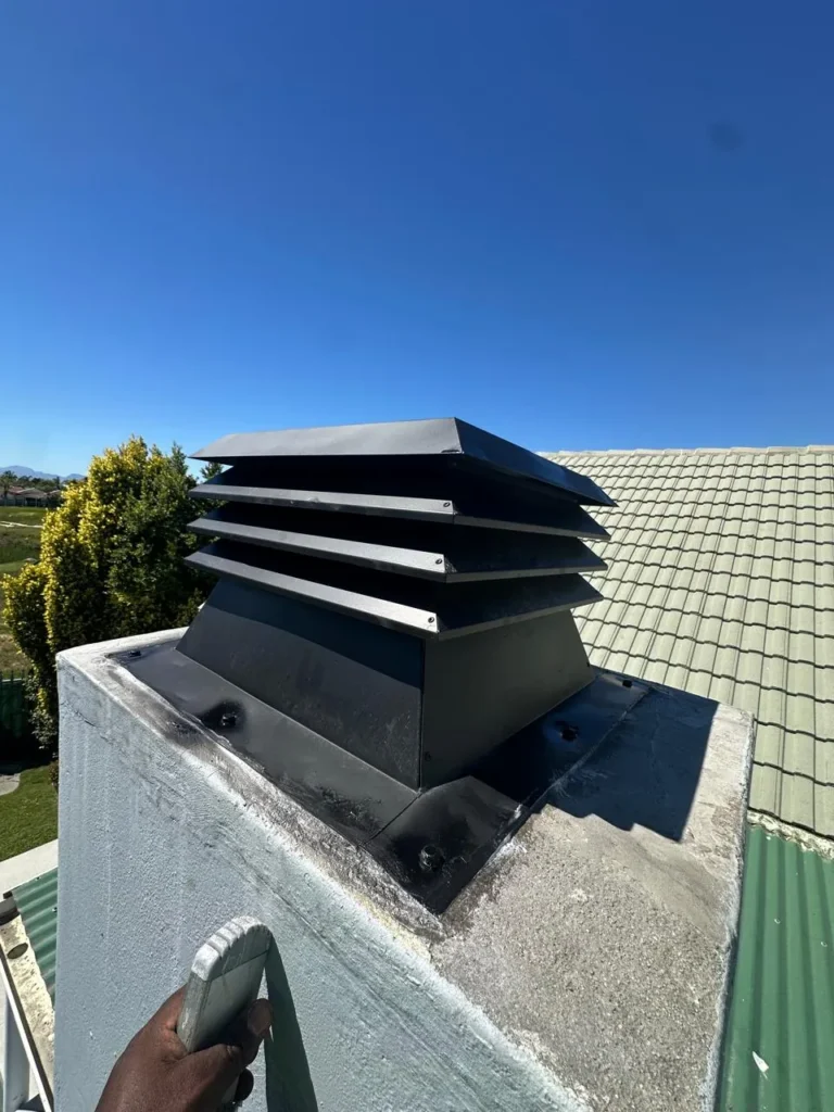 Black braai chimney cowl on a green roof, built-in braai project