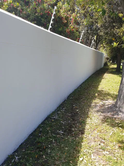 Long white painted boundary wall with an electric fence along a tree lined lawn in Hout Bay